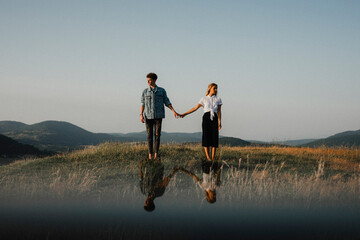 Young couple standing in nature in countryside, holding hands but looking away from each other. - Powered by Adobe