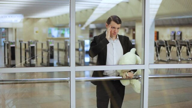 Guy is waiting on the platform with a toy bear in his hands.
