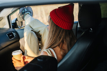 Girl in a watch cap chilling in the car, enjoying views, resting legs on window