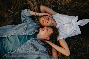 Top view of young couple on a walk in nature in countryside, lying in grass laughing.