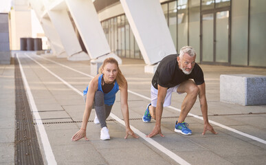 Sportive middle aged couple getting ready to start the sprint, running outdoors in urban environment