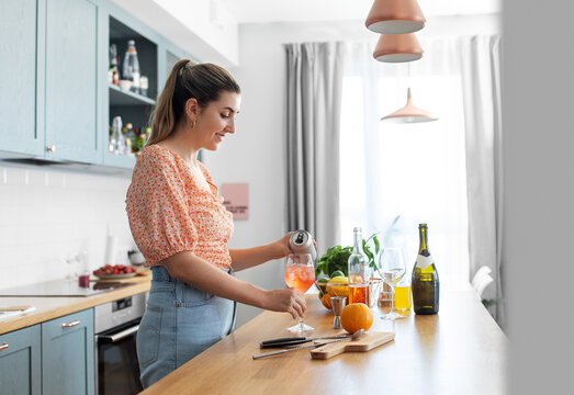 culinary, drinks and people concept - happy smiling young woman making orange cocktail at home kitchen