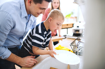 Father with down syndrome son indoors in kitchen, washing dishes.