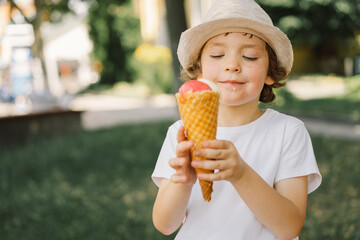 Boy in a hat is holding an ice cream and looks happy and surprised. Summer food and summer time
