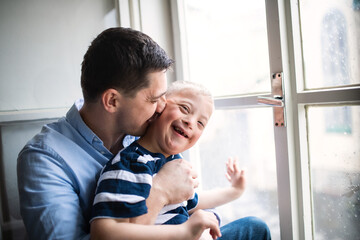 Father with happy down syndrome son indoors at home, kissing his cheek.