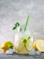 Summer refreshing ice-cold mojito or lemonade with lemon and mint on a stone white table