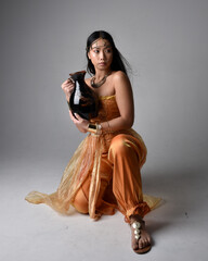 Full length portrait of pretty young asian woman wearing golden Arabian robes like a genie,...