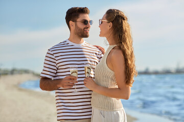 leisure, relationships and people concept - happy couple in sunglasses drinking champagne on summer beach