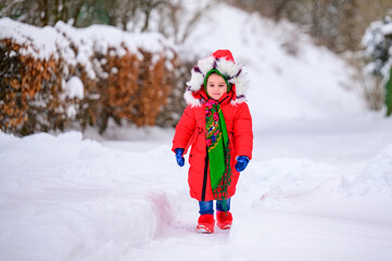 Fototapeta premium A happy girl in a red jacket and Ukrainian national kerchief walks in a snowy yard.