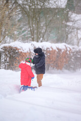 Fototapeta na wymiar Brother and sister walk in a snowy yard, having fun with snow.