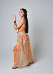 Full length portrait of pretty young asian woman wearing golden Arabian robes like a genie,...