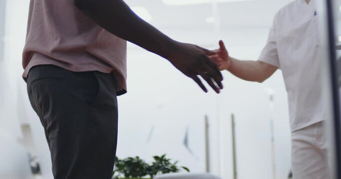An African American male patient is standing in the dental waiting room while to him came a male medical worker and they are shaking hands.