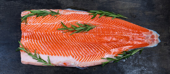 Raw trout fillet with rosemary twigs on a dark surface