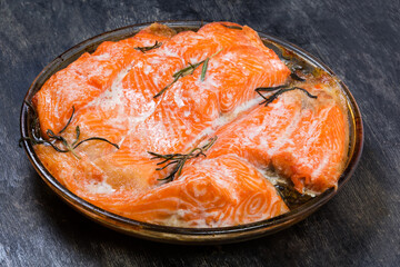 Baked trout fillet pieces on baking dish on dark surface