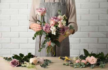 Florist creating beautiful bouquet at wooden table indoors, closeup