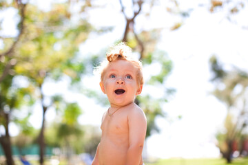 Smiling staying baby. The child is 1 year old. Surprised kid portrait . close up.portrait of pretty babe boy looking at copy space.photo on blurred background.Smiling child in forest near beach.