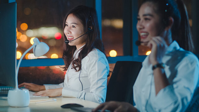 Millennial Asia young call center team or customer support service executive using computer and microphone headset working technical support in late night office. Telemarketing or sales job concept.