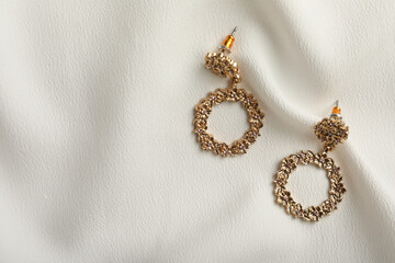 Elegant golden earrings on white fabric, flat lay with space for text. Stylish bijouterie