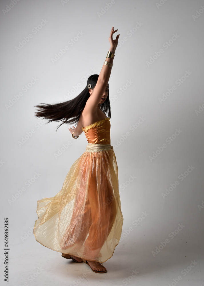 Poster Full length portrait of pretty young asian woman wearing golden Arabian robes like a genie, standing pose  with back to the camera, isolated on studio background.