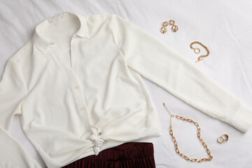 Stylish clothes and golden bijouterie on white fabric, flat lay