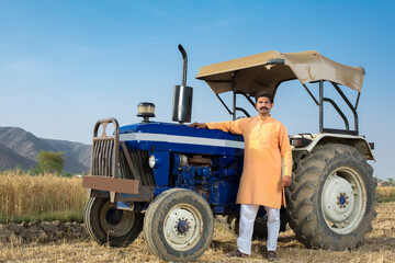 Happy Indian farmer with tractor on agricultural field