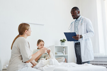 Portrait of African-American doctor talking to family in hospital room, copy space