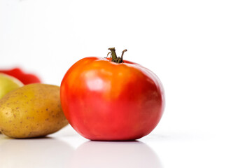 One ripe red  tomato isolated on white. Close-up. Autumn still life with tomato and potato of colorful vegetables on white background. Happy Thanksgiving. Selective focus