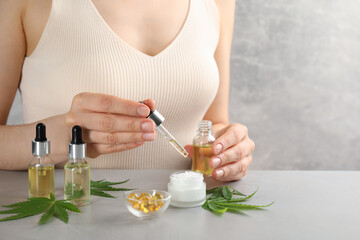 Obraz na płótnie Canvas Woman dripping THC tincture or CBD oil into cream at light stone table, closeup