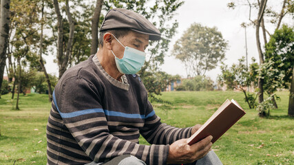 Fototapeta premium elderly man wearing a face mask to take care of himself, reading quietly in the park