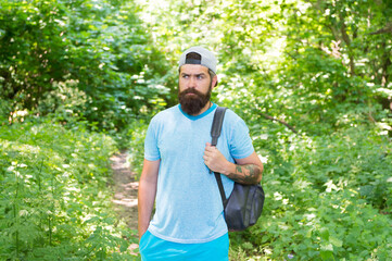 Naklejka na ściany i meble mature bearded man with beard and moustache in summer shirt and cap hold backpack in forest, sporty traveling