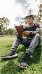 older man from latin america reading a book in the park very quietly and happily