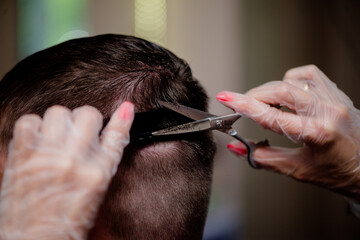 Hairdresser wearing gloves cuts a man using scissors and a hair clipper