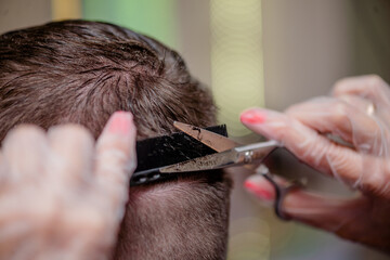 Hairdresser wearing gloves cuts a man using scissors and a hair clipper