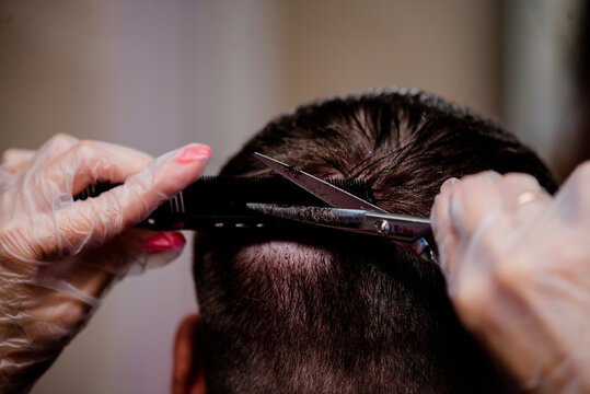 Hairdresser wearing gloves cuts a man using scissors and a hair clipper