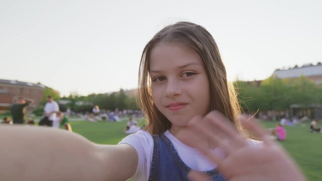 Pov shot of preteen girl taking selfie or having video call outdoors in park