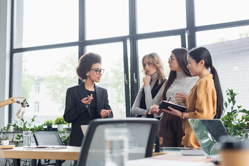 african american businesswoman gesturing while talking to multiethnic managers in office