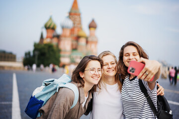 Three beautiful young woman friends making selfie using smartphone while traveling in Moscow on Red Square