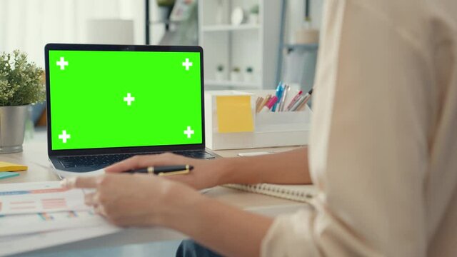 Young Asia businesswoman use smart phone with blank green screen mock up display for advertising text while smart working from home at living room. Chroma key technology, Marketing design concept.