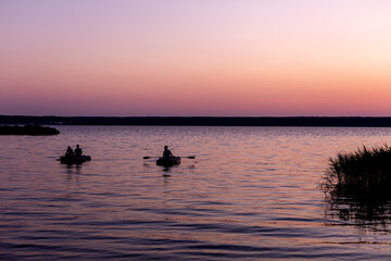 Naklejka na ściany i meble fishermen on boats swim to the shore against the background of a pink-lilac sunset on the lake