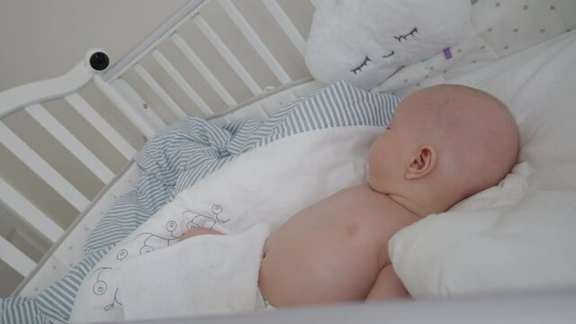 Baby boy sleeping in a crib with installed IP wireless security camera as baby monitor, interior of a modern apartment bedroom. High quality 4k footage