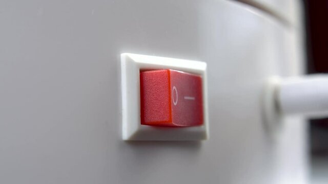 A finger pushes the red switch to the on position. Pressing the power button. Macro shot. Start electric power supply concept. White appliance
