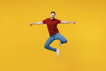 Fototapeta na wymiar Full length overjoyed fun happy young man wear red t-shirt casual clothes jump high with outstretched hands isolated on plain yellow color wall background studio portrait. People lifestyle concept