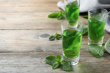 Fototapeta premium Delicious mint liqueur with green leaves on wooden table. Space for text