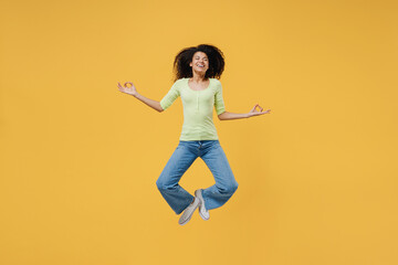 Fototapeta na wymiar Full size body length spiritual tranquil african american young woman 20s wear green shirt jump hold spread hands in yoga om aum gesture keep eyes closed isolated on yellow background studio portrait