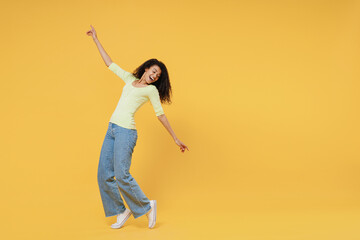 Full size body length smiling overjoyed african american young woman 20s wears green shirt standing on toes dancing lean back have fun spreading hands isolated on yellow background studio portrait