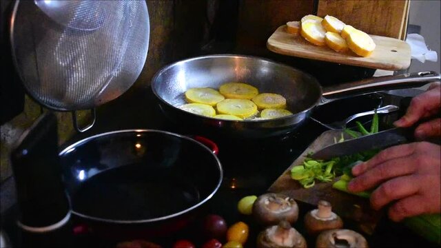 Frau schneidet Lauch in der K&uuml;che, Pfanne mit Lauch und Pfanne mit Zucchinischeiben sichtbar, kochen
