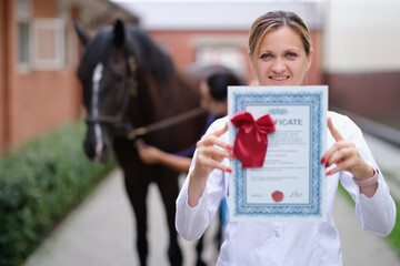 Woman veterinarian holding training certificate on horse background