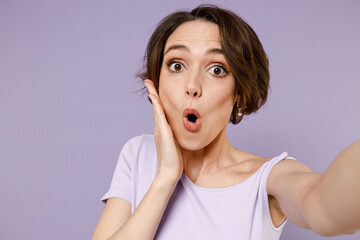 Close up young surprised happy impressed woman 20s with bob haircut wearing white t-shirt doing selfie shot on mobile cell phone camera hold face isolated on pastel purple background studio portrait.