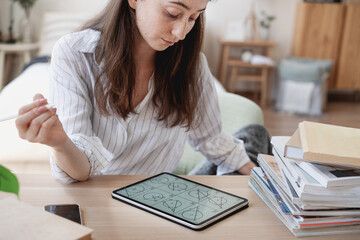 Young beautiful female student with digital tablet studying solving geometry. Online education,...