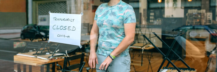 Thoughtful man with a mask behind the glass of his restaurant closed by covid-19